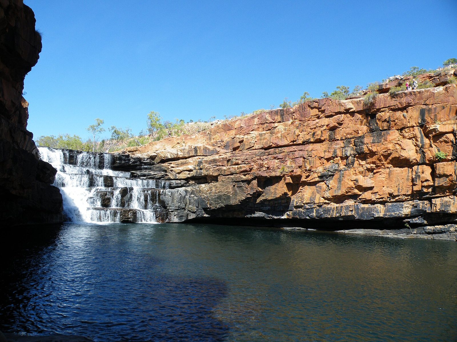 Waterfall tumbling over red rock ledges into the pool at Bell Gorge
